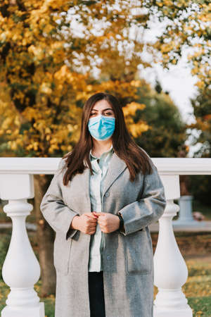 Portrait of a beautiful adult young woman on the background of autumn in the Park in a medical face maskの写真素材