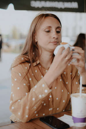 A young adult woman eats a Burger in a street cafeの写真素材