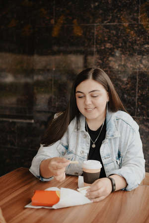 A young adult woman eats a Burger in a street cafe