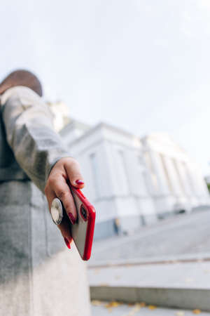 Girl with a red cell phone in hand in a cityscape. Phone close up