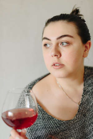 close-up of a girl in a grey sweater with a glass of red wineの写真素材