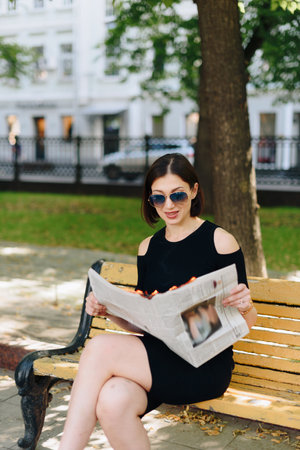 Beautiful woman in a black dress in a park with a burning newspaper in her handsの写真素材