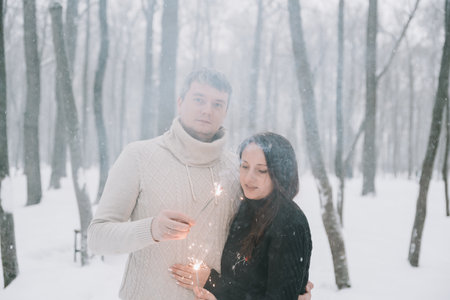 A man and a woman with sparklers on the background of a snow-covered forest in a snowfallの写真素材