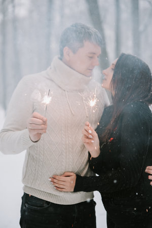 A man and a woman with sparklers on the background of a snow-covered forest in a snowfallの写真素材