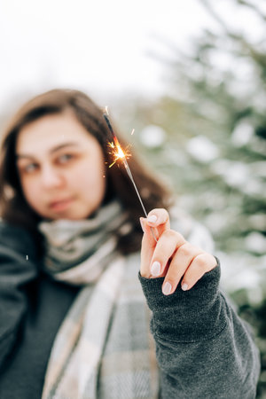 Adult young woman with sparklers on the background of winter pine forestの写真素材