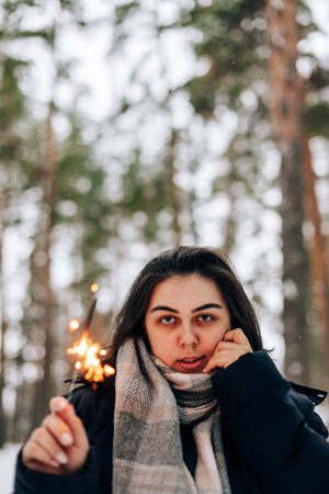 Adult young woman with sparklers on the background of winter pine forestの写真素材
