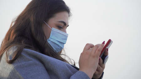A young woman with a phone in her hands wearing a maskの写真素材