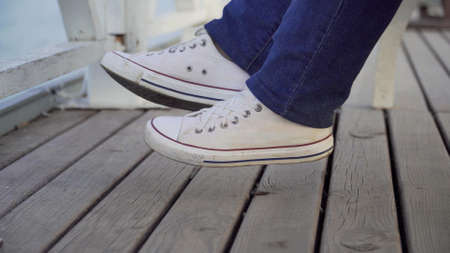 The legs of a woman sitting on a park bench in white sneakersの写真素材