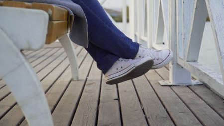 The legs of a woman sitting on a park bench in white sneakersの写真素材