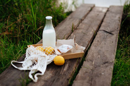 A bottle of milk and a string bag with fruit on wooden boards on the lakeの写真素材