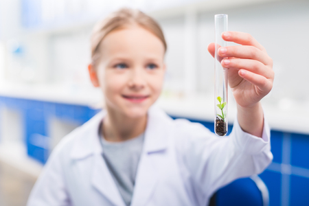 Nature in vial. Selective focus of transparent glass vial where plant growing carried by little girlの写真素材