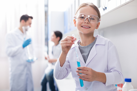 Cheerful energetic girl wearing safety glasses while holding vial and smiling to cameraの写真素材
