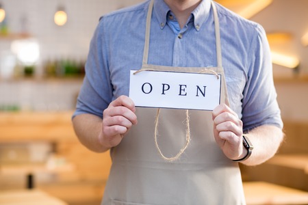 Opening sign. Close up of a label tag with an inscription open being in hands of a nice handsome cafe workerの写真素材