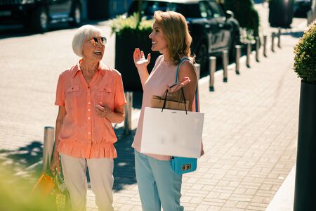Woman with shopping bags putting hands up while standing with mother