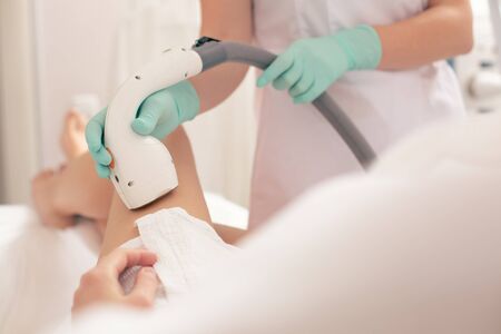 Close up photo of the modern apparatus for laser hair removal in hand of beautician wearing rubber glovesの写真素材
