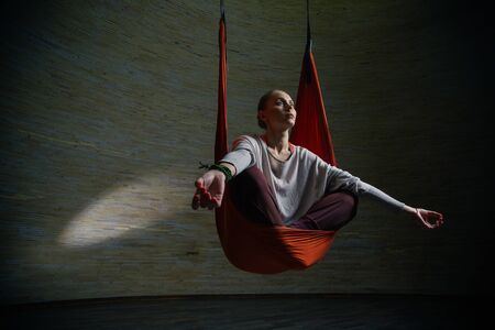 Serious woman looking into the distance while practicing aerial yoga