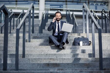 Positive bearded businessman sitting on the staircasesの写真素材
