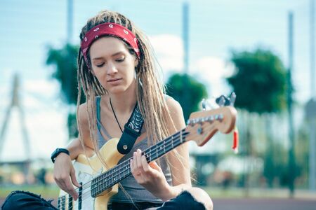 Thoughtful young lady sitting alone and playing the guitarの写真素材