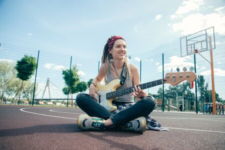 Happy musician looking glad while relaxing on sports ground with guitar
