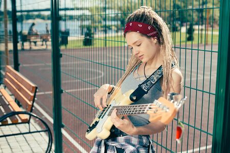 Calm lady looking at the guitar while playing it at the sports groundの写真素材