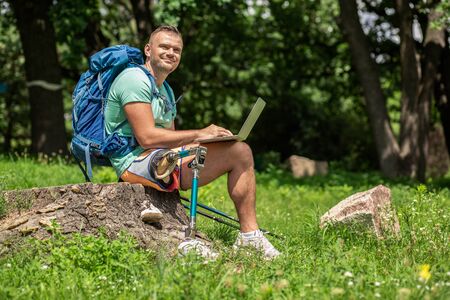 Joyful man with prosthesis using laptop outdoorsの写真素材