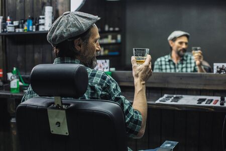 Close up of calm man in flat cap looking at the glass of alcoholの写真素材