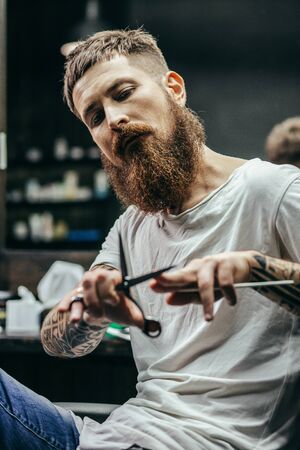 Thoughtful barber sitting and touching his scissors