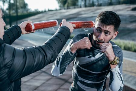 Careful boxer looking at the boxing sticks while having his training