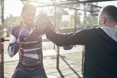 Young man wearing focus mittens and professional MMA boxer mastering his punches