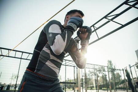 Professional MMA sportsman standing at the sports ground alone and putting fists up while performing...