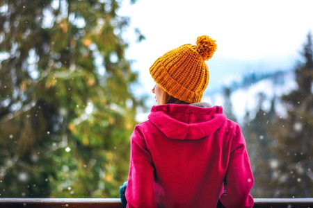 snowy weather, girl standing back in the winter, in the yellow and red knitted hat sports hooded sweatshirt. He is looking at the snowの写真素材