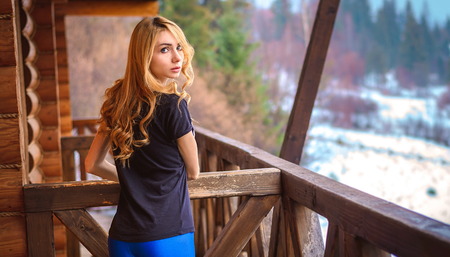 girl with long curly hair, light wheat color is on the balcony of a wooden house in the woodsの写真素材