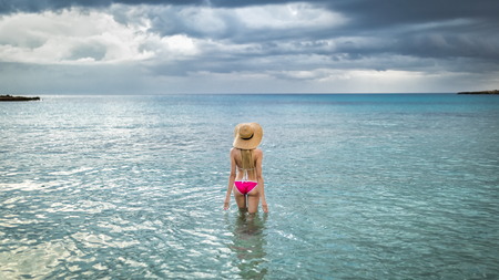 Beautiful tourist woman in straw hats for summer in a rose swimsuit stands in blue water Hawaii,...
