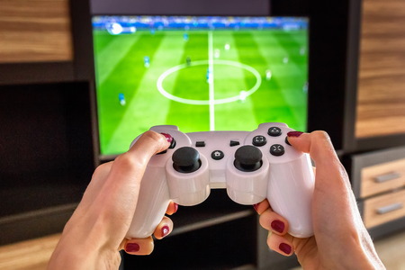 White gaming joystick, gamepad, standard controller is aimed at the TV,  Pc games is on the screen.