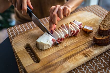 lard of a pig on a wooden board, a knife in a female hand in the kitchen