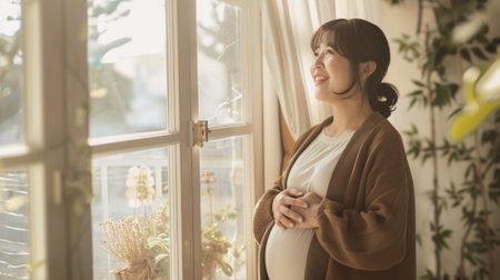 Beautiful asian pregnant woman looking out the window at home.の素材