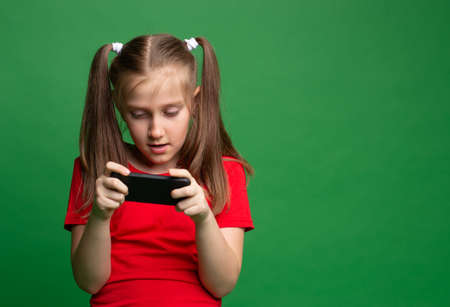 cheerful excited pretty nice girl teenager holding phone playing the game or sending a message on green color background.の写真素材