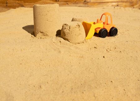 plastic toy tractor with bucket building sand towers in the sandbox. Space for textの写真素材