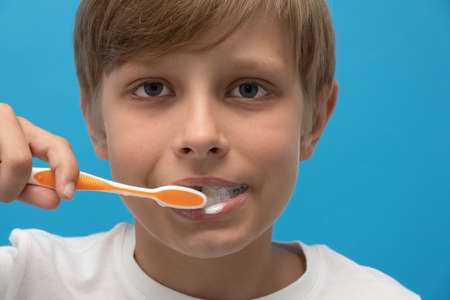 close up photo blond boy with toothbrush and toothpaste brushing his teeth.の写真素材
