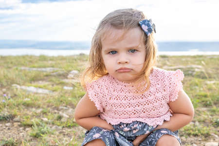 Little offended girl with chubby cheeks and plump lips. child squats in nature. Childrens emotions,...
