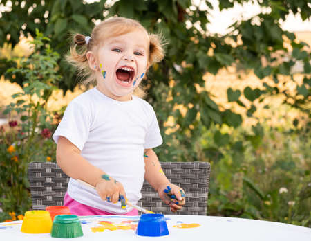 Little child drawing with paint and brush. Cute small girl painting picture in garden, outdoors at home in backyard.の写真素材