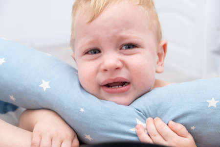 blonde baby boy crying hugging a pillow.の写真素材