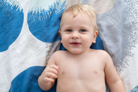 Cute blonde toddler boy lies on bed and smiles.の写真素材