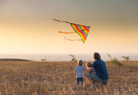 dad and kids boys fly a kite at sunset.の写真素材