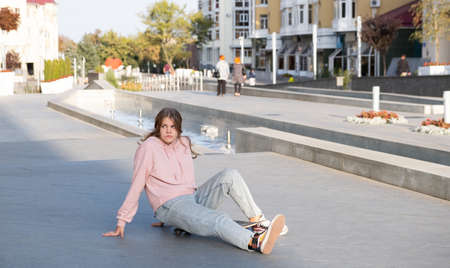 Young alternative teenager girl skater sitting on board on the city street looking away.の写真素材
