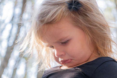 Sad toddler baby blonde girl with pouty lips looking down. unhappy childhood concept.