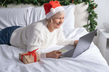 Christmas online greetings. happy senior women in Santa hat at home in bed