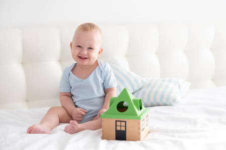 adorable happy baby boy sits on bed and play with a toy sorter.