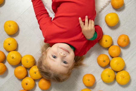 closeup portrait blonde toddler girl surrounded by a Mandarin shows different funny emotions.の写真素材
