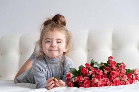 little girl lying on bed with bouquet of pink roses.の写真素材